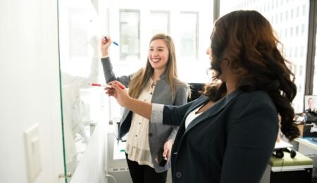two women in front of dry erase board